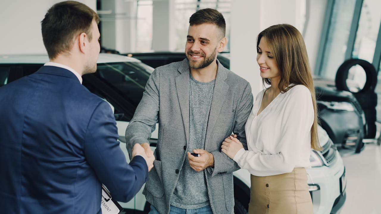Happy couple finalizing car purchase with salesman in dealership showroom. Bright and welcoming environment.